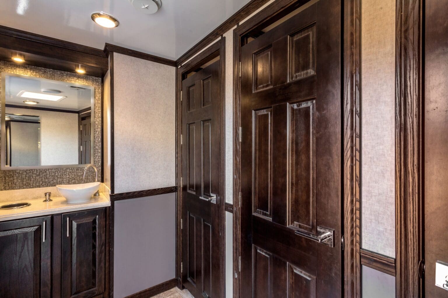 Wood vanity, vessel sink and paneled stall doors inside a VIP To Go trailer