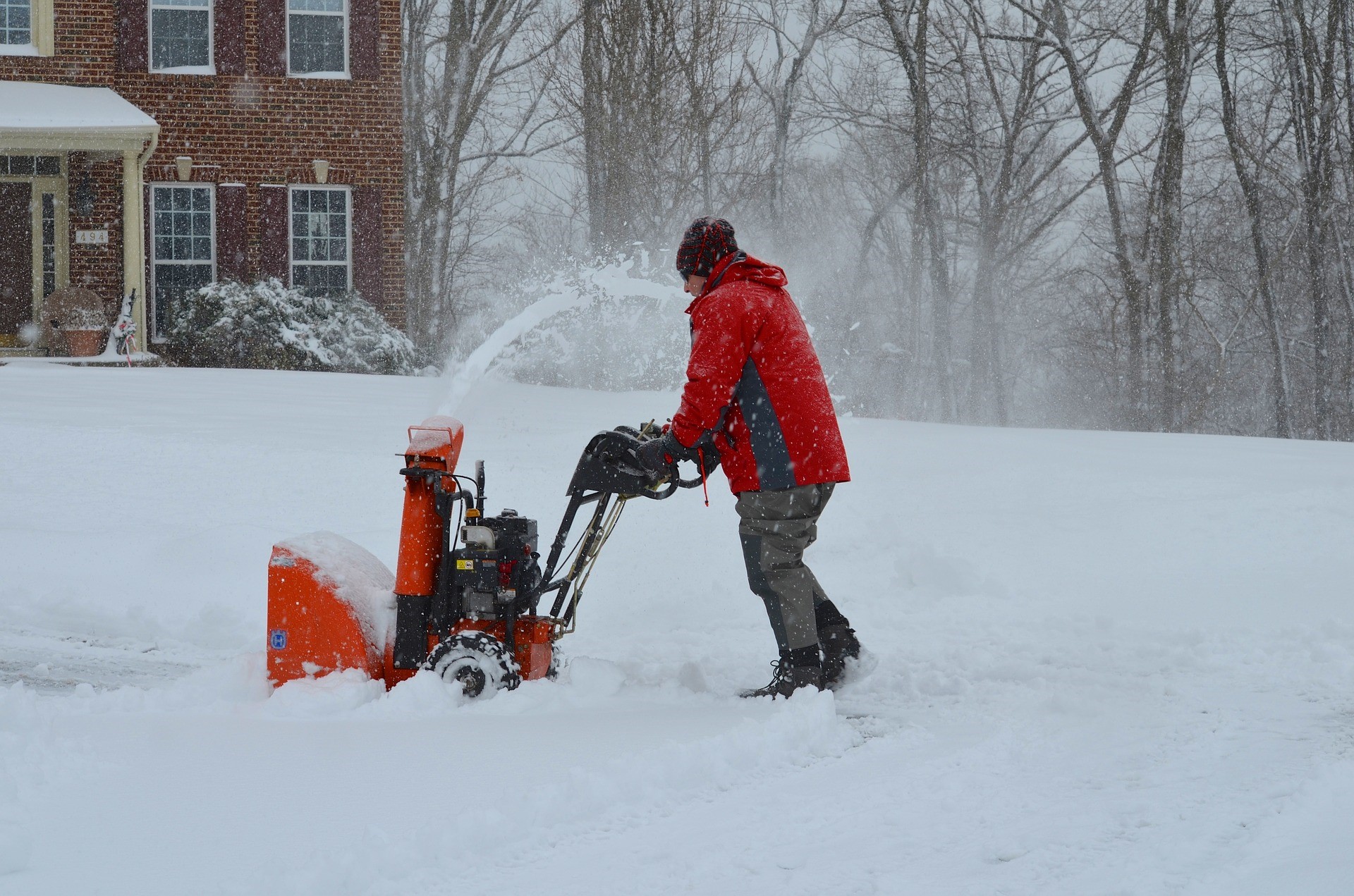 man pushing snow blower outside home